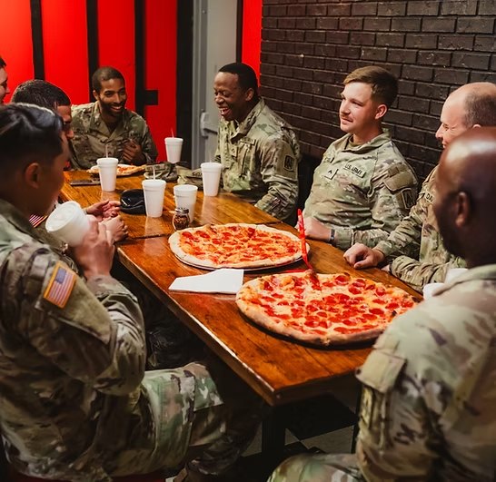 Soldiers from Fort Campbell sharing two pepperoni pies at the long table