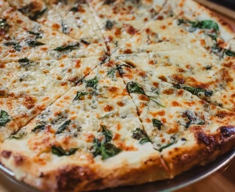 A white pie with spinach, baked golden with no red sauce